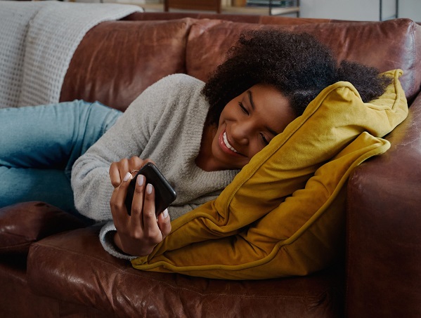 A person smiles while reclining on a couch looking at a mobile phone