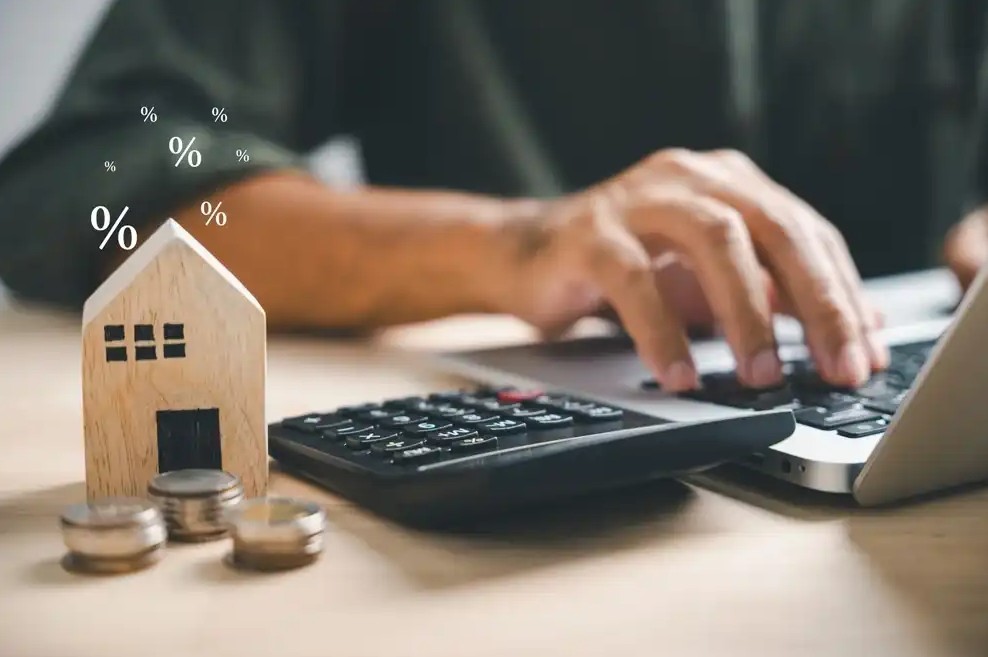 A person refinancing their loan at a computer next to a wooden house