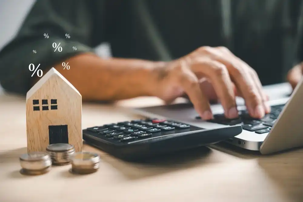 A man refinancing a loan on their computer next to a wooden house model