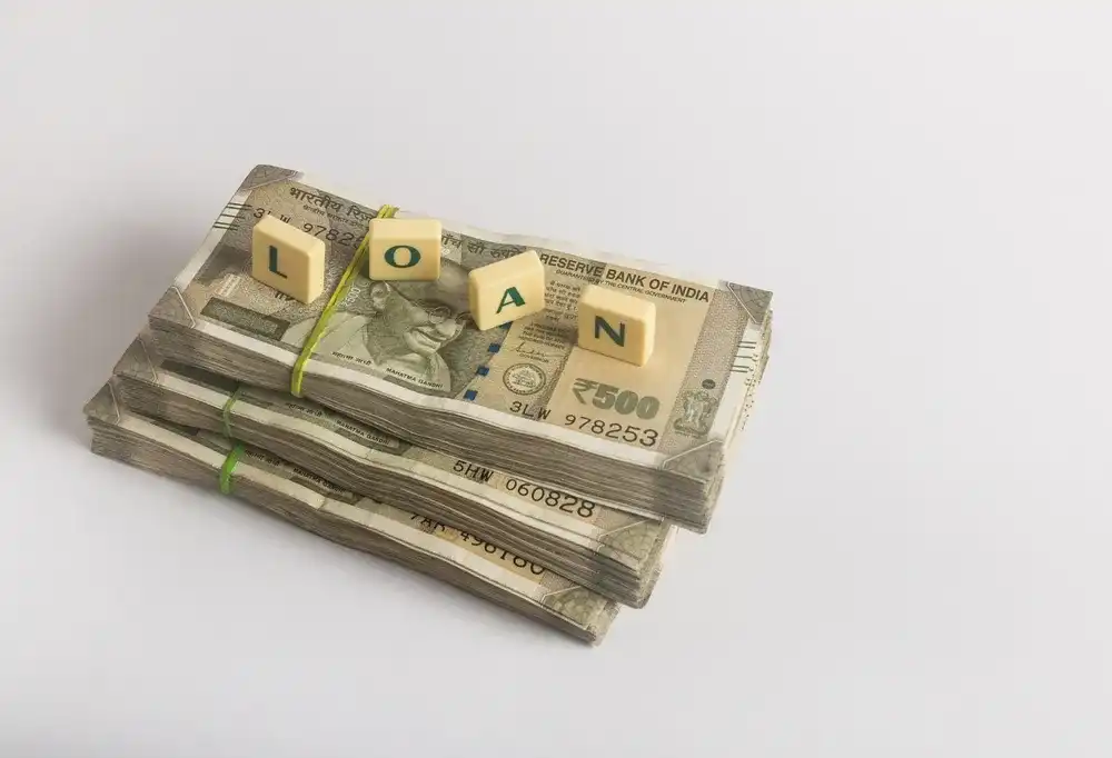 Letter blocks that spell out "Loan" atop a stack of money