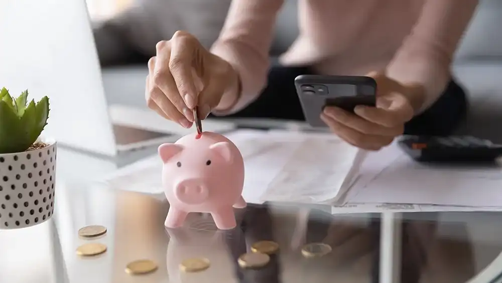 Someone depositing change in a piggy bank while on their phone